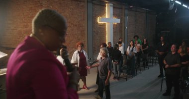 Papaz, kilise ayini sırasında dinleyiciler arasından katılımcıları çağırıyor. Ruhani liderlik, bağlılık ve modern evanjelik ibadete katılım anı.