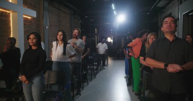 Bir Hıristiyan kilise etkinliği sırasında ayakta duran cemaat üyeleri, arka planda parlayan bir haçla ruhsal bir yansımayla meşgul oldular.