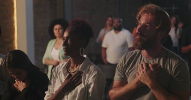 Manevi toplantı sırasında elleri göğsünde dua eden bir adam, çeşitli cemaatlerle çevrili, yanında dua eden Afrikalı Amerikalı bir kadın, inanç ve bağlılık vurgulandı