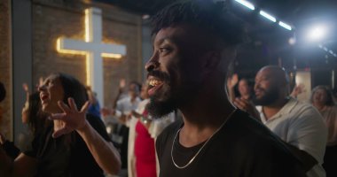 Kiliseye ibadet sırasında alkış tutan ve gülümseyen çok kültürlü cemaat, arka planda aydınlatılmış haç, inanç, neşe, birlik ve ruhani bağlılık ifadeleri.