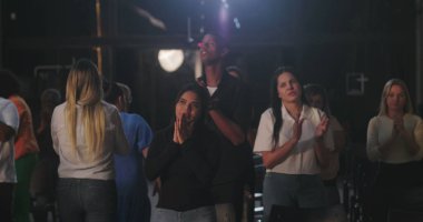 Cemaat el çırparken ve koltuklara otururken insanlar el kaldırıyor, kameralar duvardaki aydınlatılmış haça doğru dönüyor, inanç, bağlılık ve birliği ifade eden ruhani bir toplantı.