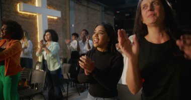 Kilisede ibadet sırasında alkışlayan ve gülümseyen çeşitli insanlar, arka planda parlayan haç, neşe, birlik ve ruhsal bağlantı ifadeleri