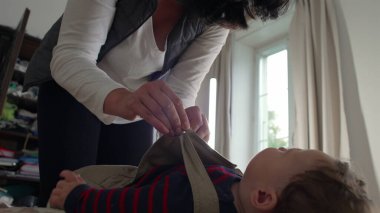 Anne bebek tulumlarını bağlıyor, bebek yatakta sakin kalırken kayışları ayarlıyor, günlük rutin rutin işlerinde rahat bir evde bakım ve bakım yapıyor..