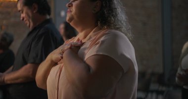 Çeşitli grup ibadetleri sırasında dua eden elleri havada, gözleri kapalı, arka planda ışık saçan kadın, maneviyat ve bağlantı vurgulandı