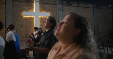 İçten ibadete katılan bireyler ellerini kaldırmış, arka planda haç aydınlatmış, kilise ayini sırasında sadakat, birlik ve inanç ifadeleri sergiliyorlar.