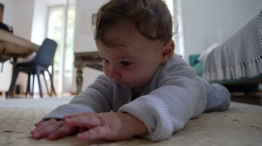 Bebek yerde yatıyor, ellere odaklanıyor, çevreyi keşfediyor, dokunsal oyunlar oynuyor, iyi motor becerilerin gelişimi, ev ortamında sessiz bir konsantrasyon anı..