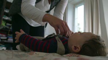 Anne bebek tulumlarını bağlıyor, bebek yatakta yatarken yakın çekim eller kayışları ayarlıyor, anne ve bebekle sıcak bir odada sabah rutininde sakin bir etkileşim..