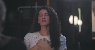 Minnettarlığını ifade eden kıvırcık saçlı kadın, gözleri kapalı, elleri göğsüne bastırılmış, huzurlu ve duygusal yansıma sırasında.