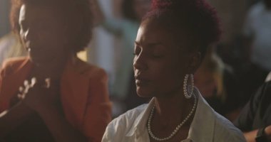 Cemaat, elleri göğsünde, gözleri kapalı, derin inanç ve ruhani bağlılıklarını ifade eden, arka planda birlikte ibadet eden farklı insan grupları, Hıristiyan ruhaniliği