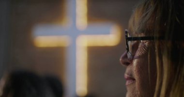 İbadet sırasında huzur içinde dua eden yaşlı kadın, arka plan, inanç, maneviyat ve içgözlem konularında aydınlatılmış haç,