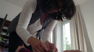 Anne bebek tulumlarını bağlıyor, bebek yatakta sakin kalırken kayışları ayarlıyor, günlük rutin rutin işlerinde rahat bir evde bakım ve bakım yapıyor..