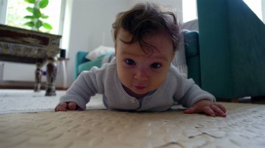 Bebek yerde, kollarıyla yukarı itiyor, merakla ileriye bakıyor, oturma odasında etkin bir şekilde etrafı keşfediyor, emeklemeyi öğrenmenin ilk aşamaları..