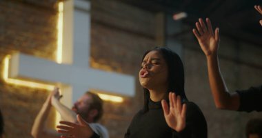 Odaklanmış, duada el kaldıran, derin ruhsal bağ kuran, Hıristiyan inancı olan, ibadet eden, arka planda aydınlanan haç, ibadette birlik, dini bağlılık