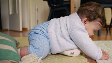 Bebek paspasın üzerinde oturuyor, ellerle çevreyi keşfediyor, merak ve odak ile dokunsal oyunlara girişiyor, ev ortamında erken çocukluk gelişimi.