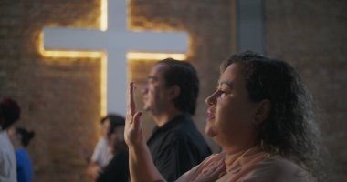 Çeşitli grup ibadetleri sırasında dua eden elleri havada, gözleri kapalı, arka planda ışık saçan kadın, maneviyat ve bağlantı vurgulandı