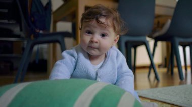 Bebek yerde oturuyor, tuhaf bir ifadeyle yukarı bakıyor, sıcak bir ev ortamında destek için ellerini kullanıyor, tamamen gözlem altında..