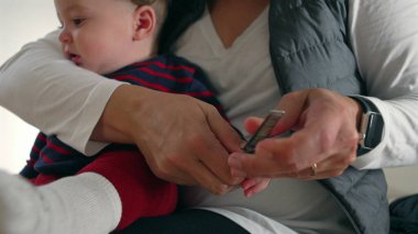 Anne, bebeğin tırnaklarını dikkatlice keserken kucağında kişisel bakım, bakım, bakım ve odaklanmış ebeveynlik yapıyor..