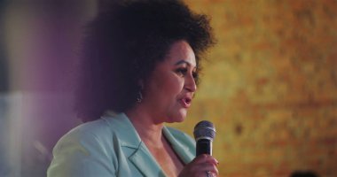 Mikrofona konuşan bir kadının, ilham verici bir ruhani etkinlik, toplum liderliği ve inanç sırasında tutku ve otorite ile dinleyicilere seslenişi.