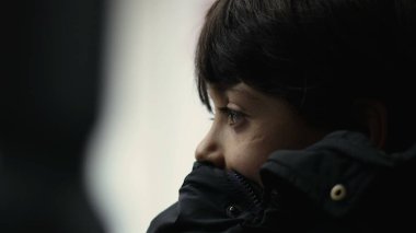 Ceketin üzerinde dinlenen genç bir çocuğun yakın çekimi, hareket halindeki otobüsün önünden geçen manzaraya bakmak, ciddi bir ifade, sessiz bir an, düşüncelere dalmış, derin bir düşünce.