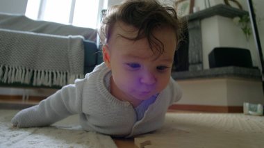 Bebek yerde yatıyor, kollarıyla yukarı itiyor, çevreyi keşfediyor, merakla bekliyor, oyuncaklarla çevrili bir evde, emeklemeyi öğrenmenin ilk aşamalarında.