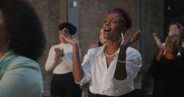 Çeşitli bireylerden oluşan bir grup, duvarlarla çevrili bir ortamda alkışlıyor ve tezahürat yapıyor. Odaklanmış ifadeler, birlik hissi, el çırpma üzerine yakın çekim.