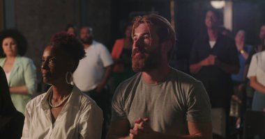 Manevi toplantı sırasında elleri göğsünde dua eden bir adam, çeşitli cemaatlerle çevrili, yanında dua eden Afrikalı Amerikalı bir kadın, inanç ve bağlılık vurgulandı