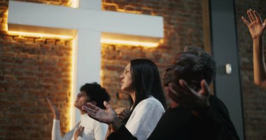 Kilisede el kaldırarak ibadet eden çeşitli gruplar, birliğe olan inanç ve bağlılıklarını ifade eden, arka planda aydınlanan haç ruhaniliği simgeliyor.