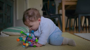 Bebek yerde oturuyor, neşeli bir oyuncakla oynarken neşeyle gülüyor, neşeli ve eğlenceli bir keşifle meşgul, sıcak bir ev ortamında eğlenceli aile vakitlerinin tadını çıkarıyor..