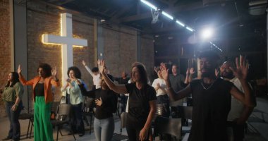 Çeşitli cemaatler kilise ayini sırasında el kaldırıyor, arka planda haç ışığı, ruhsal bağlantı ve kutsal mekanda kolektif bağlılık.