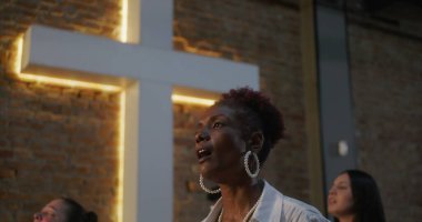 İbadet sırasında insanlar tutkuyla ve inançla şarkı söylüyor. Aydınlanmış haçın önünde duruyorlar. Ruhaniliği, bağlılığı ve toplumsal bağlantıyı temsil ediyorlar.