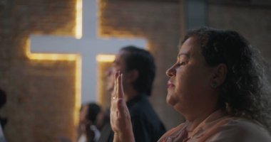 Çeşitli grup ibadetleri sırasında elleri kalbimde olan kadın, arka planda aydınlatılmış haç, maneviyat, inanç ve minnettarlık vurgulandı