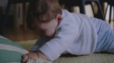 Bebek yerde yatıyor, çizgili bir yastığa uzanıyor, hayal kırıklığı ve öfke belirtileri gösteriyor, dokunarak oynamaya çabalıyor, hareket becerilerini geliştiriyor..