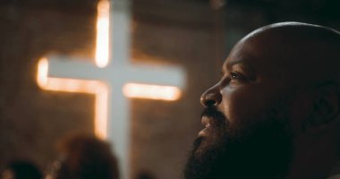 İbadet sırasında düşünceli ifadeli bir adamın profili, arka plan, inanç, maneviyat ve içgözlem konularında aydınlatılmış bir haç.