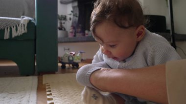 Bebek yerde oturup anne bacağına odaklanarak ve merakla dokunuyor, çevreyi keşfediyor, evde aile içi ilişkiler kuruyor, bebek ve anne arasında neşeli bir etkileşim, sakin bir yuva kuruyor..