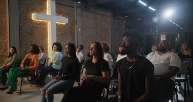 İçten bir ibadet sırasında alkış tutan cemaat, inançla ve duayla meşgul olan insanlar, tuğla bir duvarda yanan haç, ruhani bir atmosfer yaratıyor.