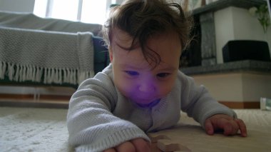 Bebek yerde yatıyor, kollarıyla yukarı itiyor, çevreyi keşfediyor, merakla bekliyor, oyuncaklarla çevrili bir evde, emeklemeyi öğrenmenin ilk aşamalarında.