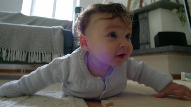 Bebek yerde yatıyor, kollarıyla yukarı itiyor, çevreyi keşfediyor, merakla bekliyor, oyuncaklarla çevrili bir evde, emeklemeyi öğrenmenin ilk aşamalarında.