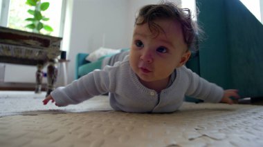 Bebek yerde, kollarıyla yukarı itiyor, merakla ileriye bakıyor, oturma odasında etkin bir şekilde etrafı keşfediyor, emeklemeyi öğrenmenin ilk aşamaları..