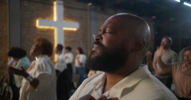 Yürekten ibadet eden bir adam, arka planda parlayan bir haç, kutsal kilisede derin manevi yansıma, inanç ve duygusal bağlantı.