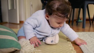 Bebek paspasın üzerinde oturuyor, ellerle çevreyi keşfediyor, merak ve odak ile dokunsal oyunlara girişiyor, ev ortamında erken çocukluk gelişimi.