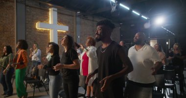 Kiliseye ibadet sırasında alkış tutan ve gülümseyen çok kültürlü cemaat, arka planda aydınlatılmış haç, inanç, neşe, birlik ve ruhani bağlılık ifadeleri.