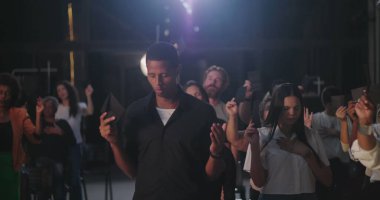 Bir grup tapan ellerinde zarflar tutarken, manevi dualarda el kaldırırken ve duygusal bir kilise toplantısında yansıtırken.