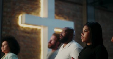 Siyahlı genç bir kadın, ciddi bir ifadeyle, arka planda aydınlanmış haç, Hıristiyan inancını, tefekküre ve çeşitli cemaatleri vurgulayan ruhani bir toplantı.