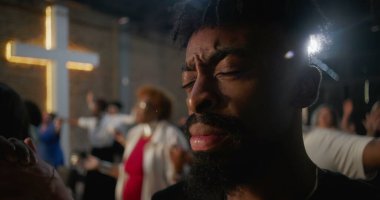 İbadet ederken el ele tutuşan, inançlarını ve bağlılıklarını ifade eden, arka planda aydınlanmış haç ruhaniliği, umudu ve yürekten birliği temsil eden bir grup insan.