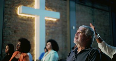 Kilisede arka planda aydınlık haçı olan bir adam, el kaldırarak dua ediyor, kapalı alanda dini hizmet veriyor, maneviyatın ifadesi, birlik ve bağlantı, topluma olan inanç.