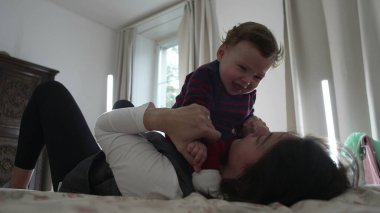 Anne yatakta ağlayan bir bebek tutuyor, duygusal bir anda rahatlatıyor ve sakinleştiriyor, sakin bir ev ortamında çocuk bakımını ve erken çocukluk gelişimini gösteriyor..