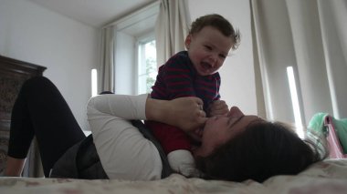 Anne yatakta ağlayan bir bebek tutuyor, duygusal bir anda rahatlatıyor ve sakinleştiriyor, sakin bir ev ortamında çocuk bakımını ve erken çocukluk gelişimini gösteriyor..