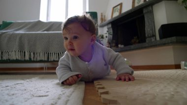 Bebek yerde yatıyor, ahşap bir bloğu yakından inceliyor, merakla eğiliyor, etkin bir şekilde çevreyi keşfediyor, erken çocukluk öğrenimi, rahat bir evde dokunsal bir keşif..