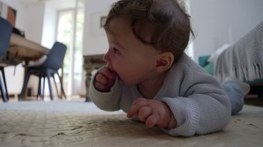 Bebek yerde yatıyor, ellere odaklanıyor, çevreyi keşfediyor, dokunsal oyunlar oynuyor, iyi motor becerilerin gelişimi, ev ortamında sessiz bir konsantrasyon anı..