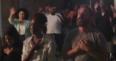 Dua eden cemaat, elleri kalplerinin üzerinde duran ve ibadet ederek büyüyen farklı gruplar, kilisedeki ruhani toplantı sırasında duygusal inanç ve bağlılık anları.